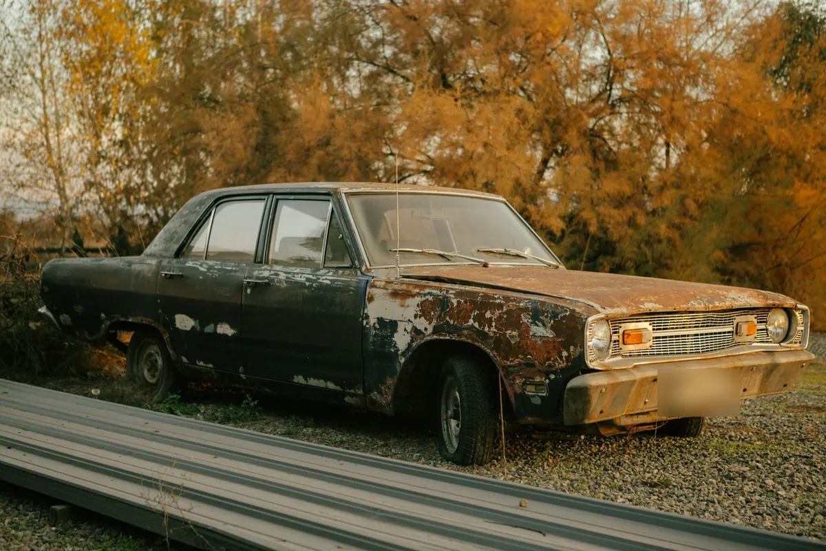 Abgestelltes älteres Auto mit Rost vor herbstlichen Bäumen